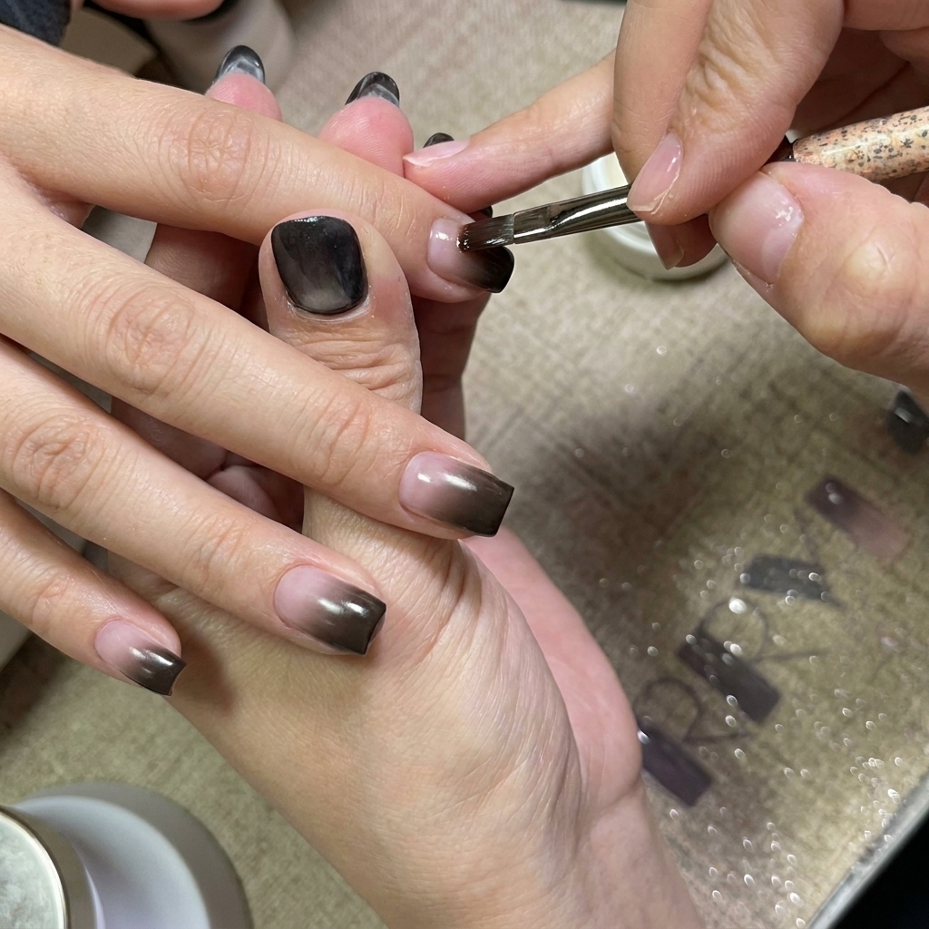 A nail brush applying a smooth coat of clear gel over the gradient nails.