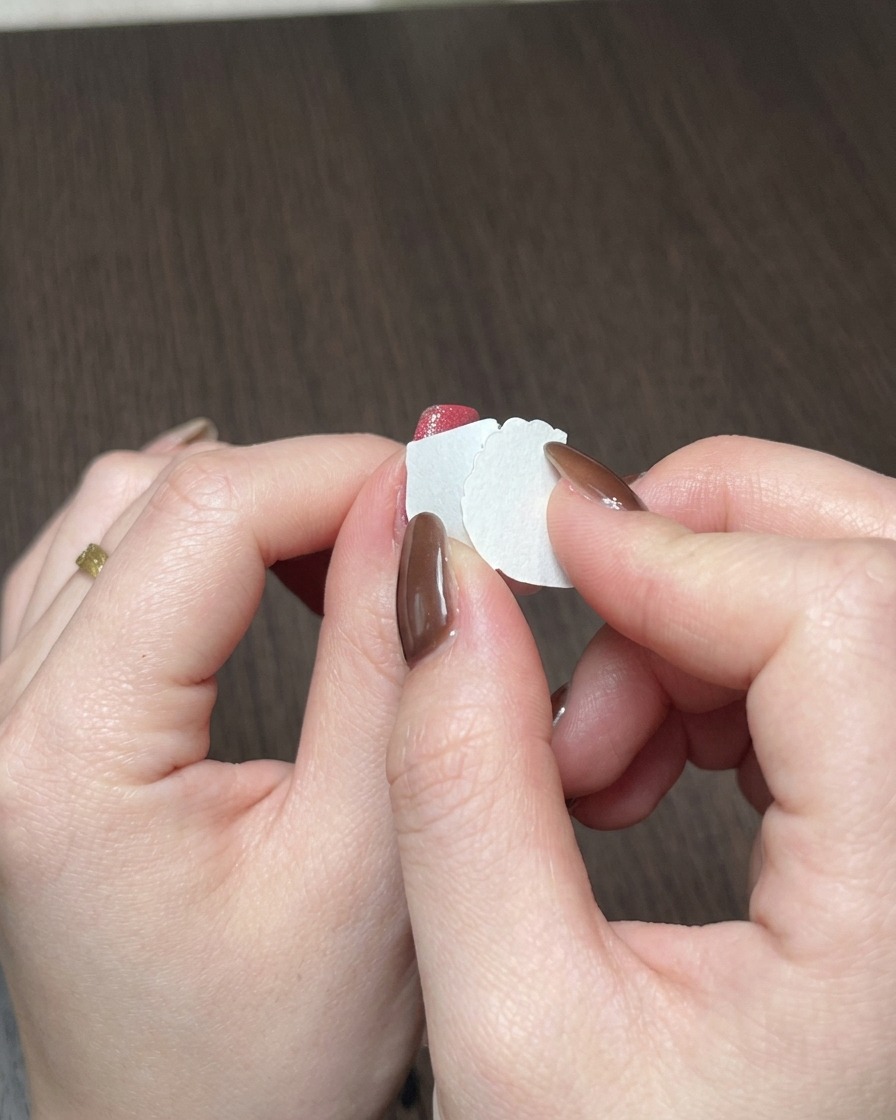 A close-up of a makeup sponge dabbing red gel polish onto the free edge of a nail.