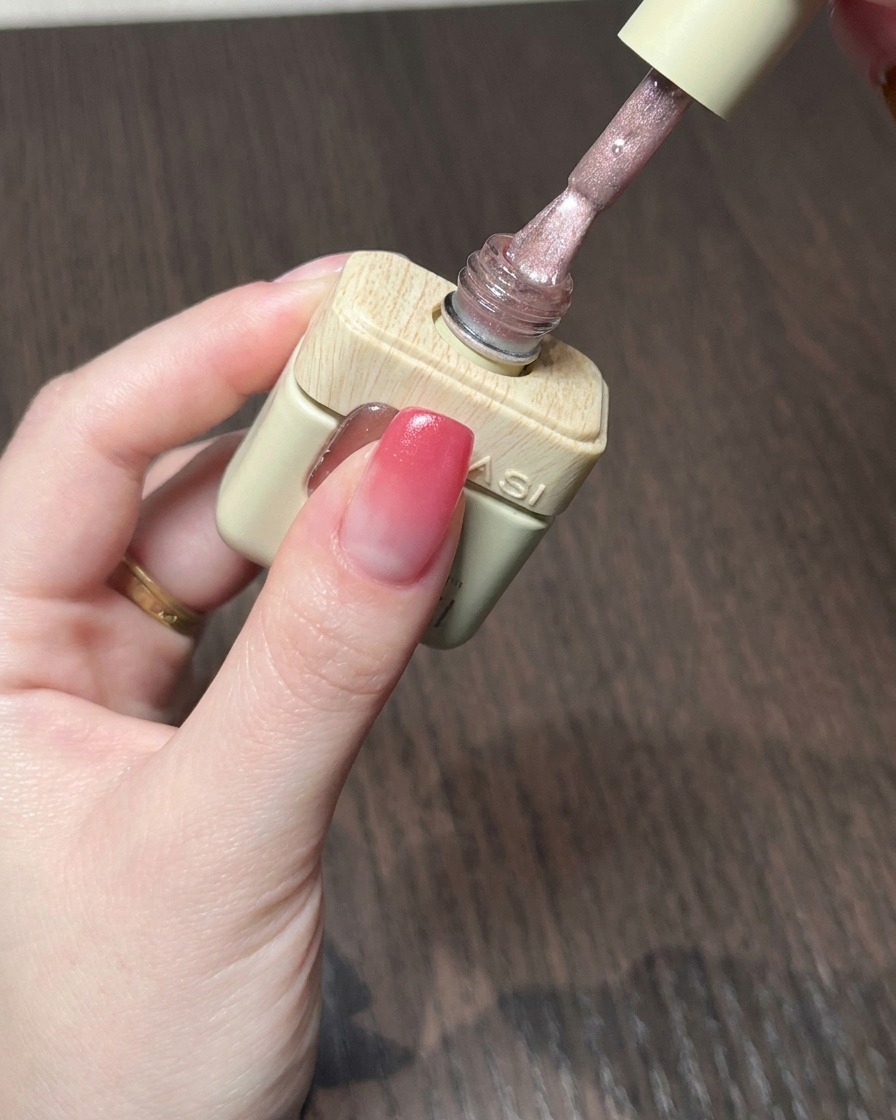 A brush applying a shimmering nude pink cat eye gel over the red gradient base.