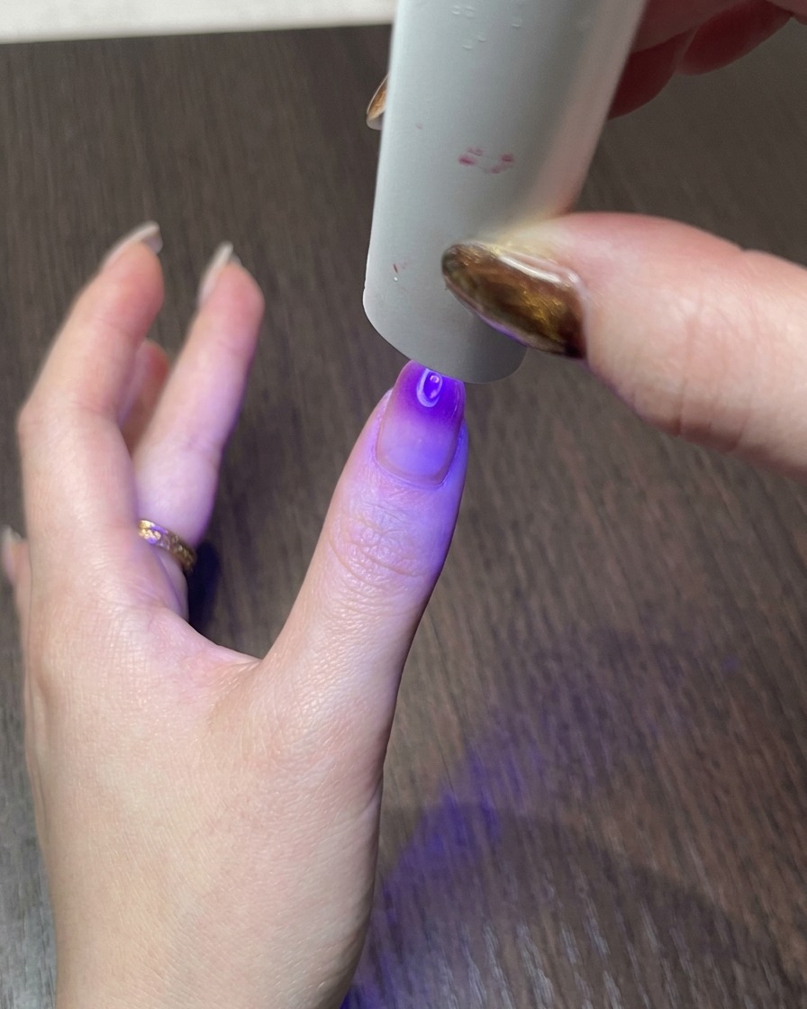 A hand under a small UV lamp, curing the finished magnetic cat eye nail design.