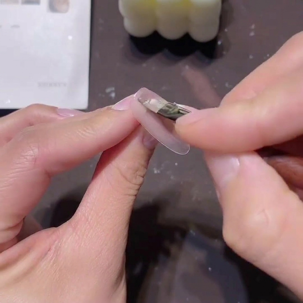 A brush applying a thin layer of sheer pink-nude gel polish onto a prepped nail.