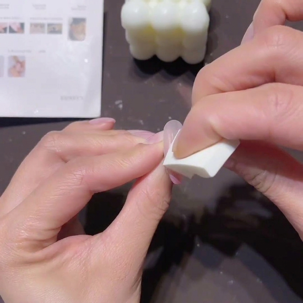 A close-up of a persons hands using a small white wedge sponge to dab peach-pink gel onto a thumbnail to create an ombre effect.