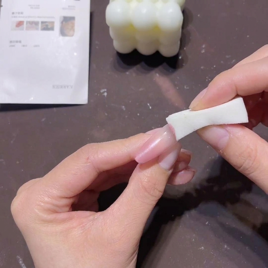 A close-up of a hand using a white sponge block to dab peach-pink gel onto the tip of a long nail to create a gradient effect.