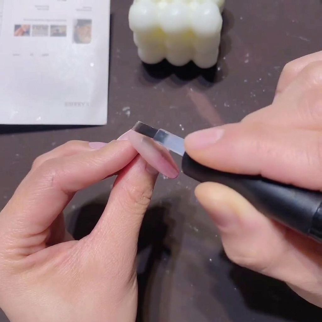 A flat nail brush applying a smooth layer of clear base coat over a pink gradient nail to seal the color.