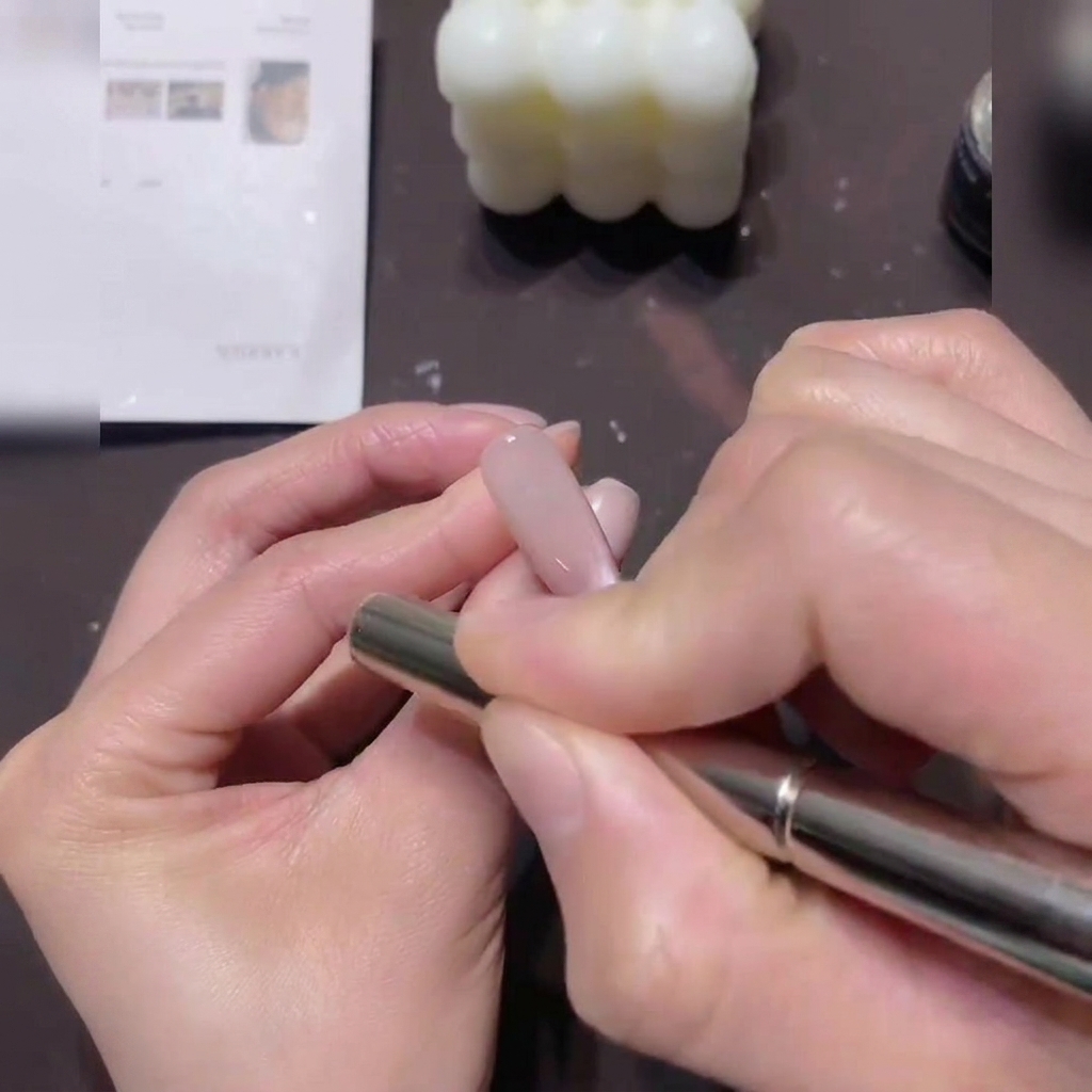 A hand holding a cylindrical magnet, hovering it in circular motions around the edge of a nail coated in cat-eye gel.