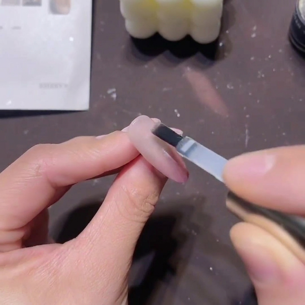 A flat gel brush applying a thick, clear builder top coat over a finished pink magnetic nail design.