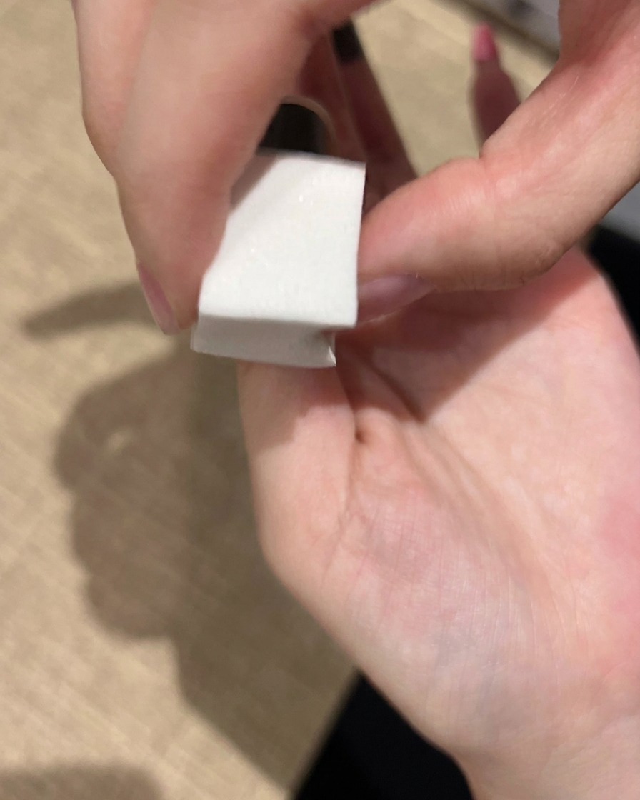 A makeup sponge being used to gently dab pink gel polish onto a fingernail to build a soft, blended gradient.