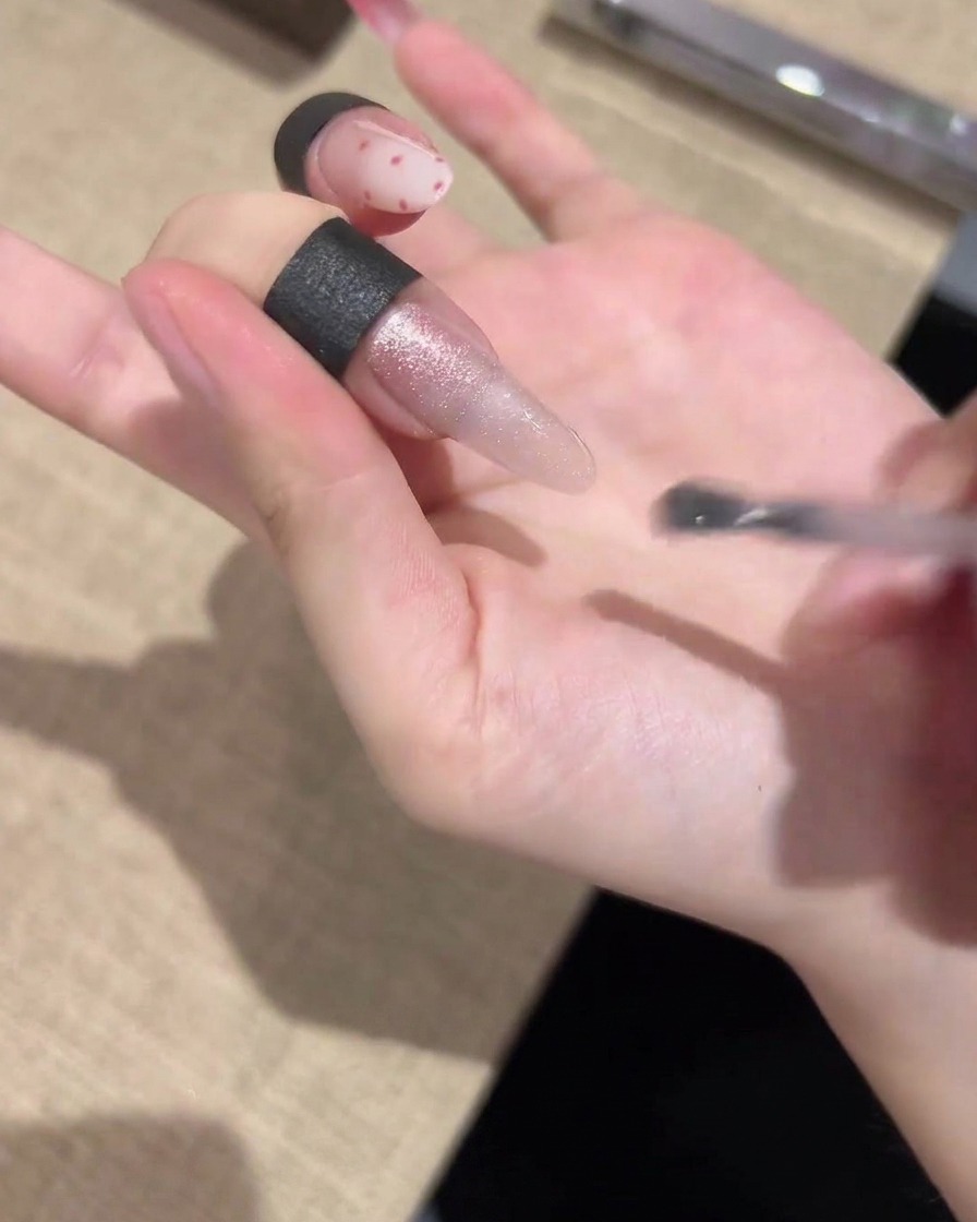 A brush applying a shimmering cat-eye gel polish uniformly across the entire length of the nail.