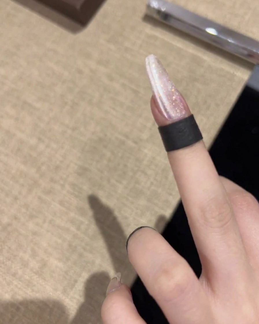 A magnetic tool held horizontally near the nail, creating a sharp, bright line through the shimmering gel polish.