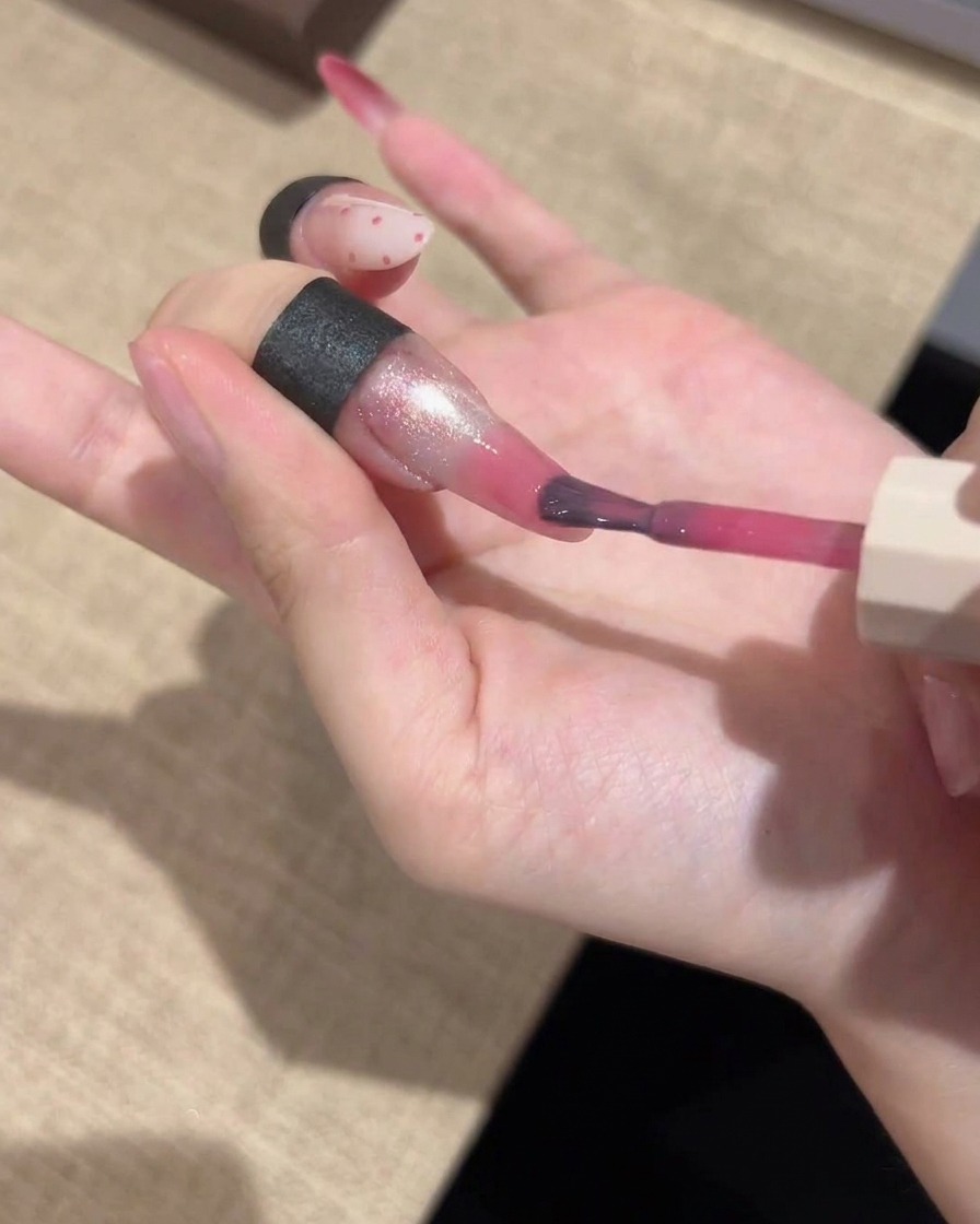 A fine-detail brush applying a vibrant pink gel color to the tips of a manicured nail, blending it for a gradient finish.