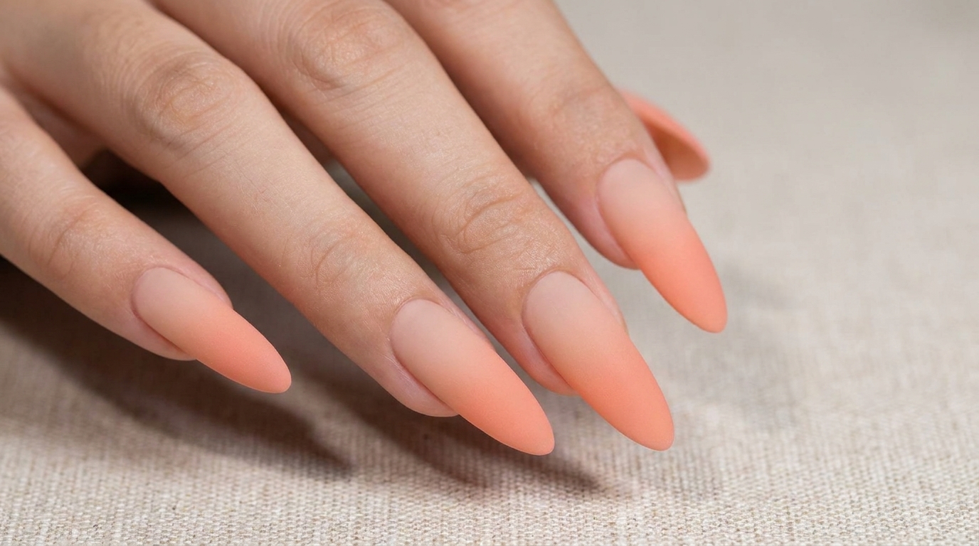 Long almond-shaped nails featuring a smooth, sophisticated peach-to-nude ombre gradient with a soft matte finish.