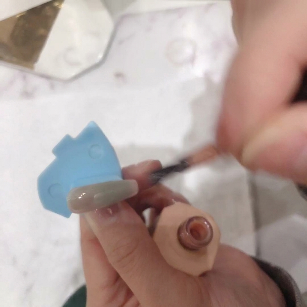 A close-up view showing the second layer of nude pink polish being applied to the nail surface.