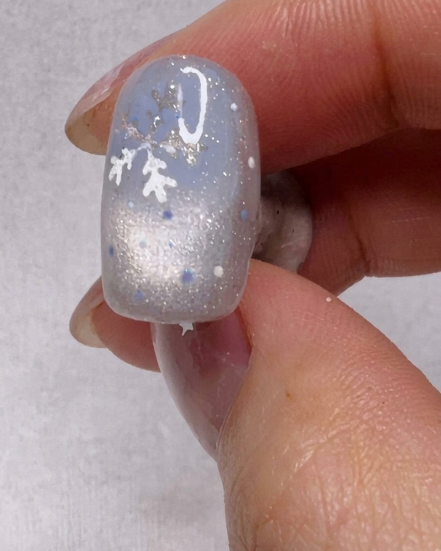 A brush applying a coat of shimmery silver gel polish to a nail.
