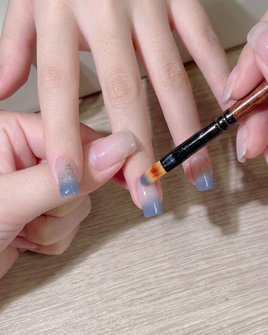 A makeup sponge dabbing light blue polish onto a fingernail.