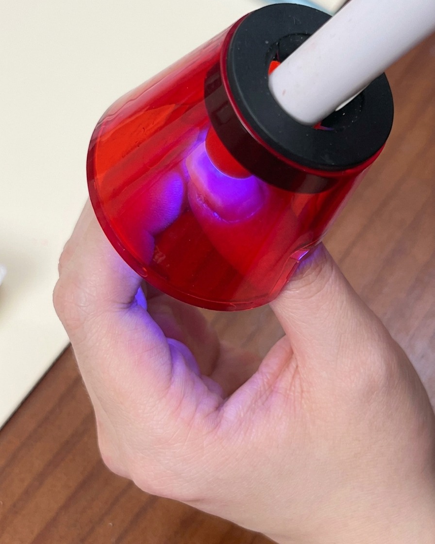 A brush applying a shimmering white cat-eye gel polish over the colorful gradient base.