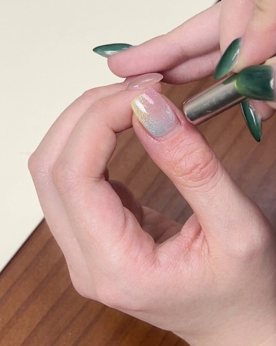 A cylindrical magnet being held near the side of a fingernail to style shimmering cat-eye gel polish.