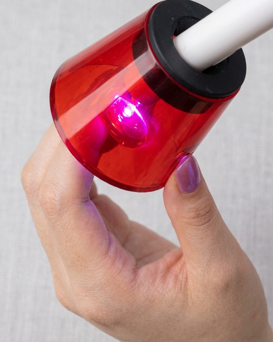 A fingernail placed under a red UV/LED lamp, curing with the cat-eye magnetic particles visible.