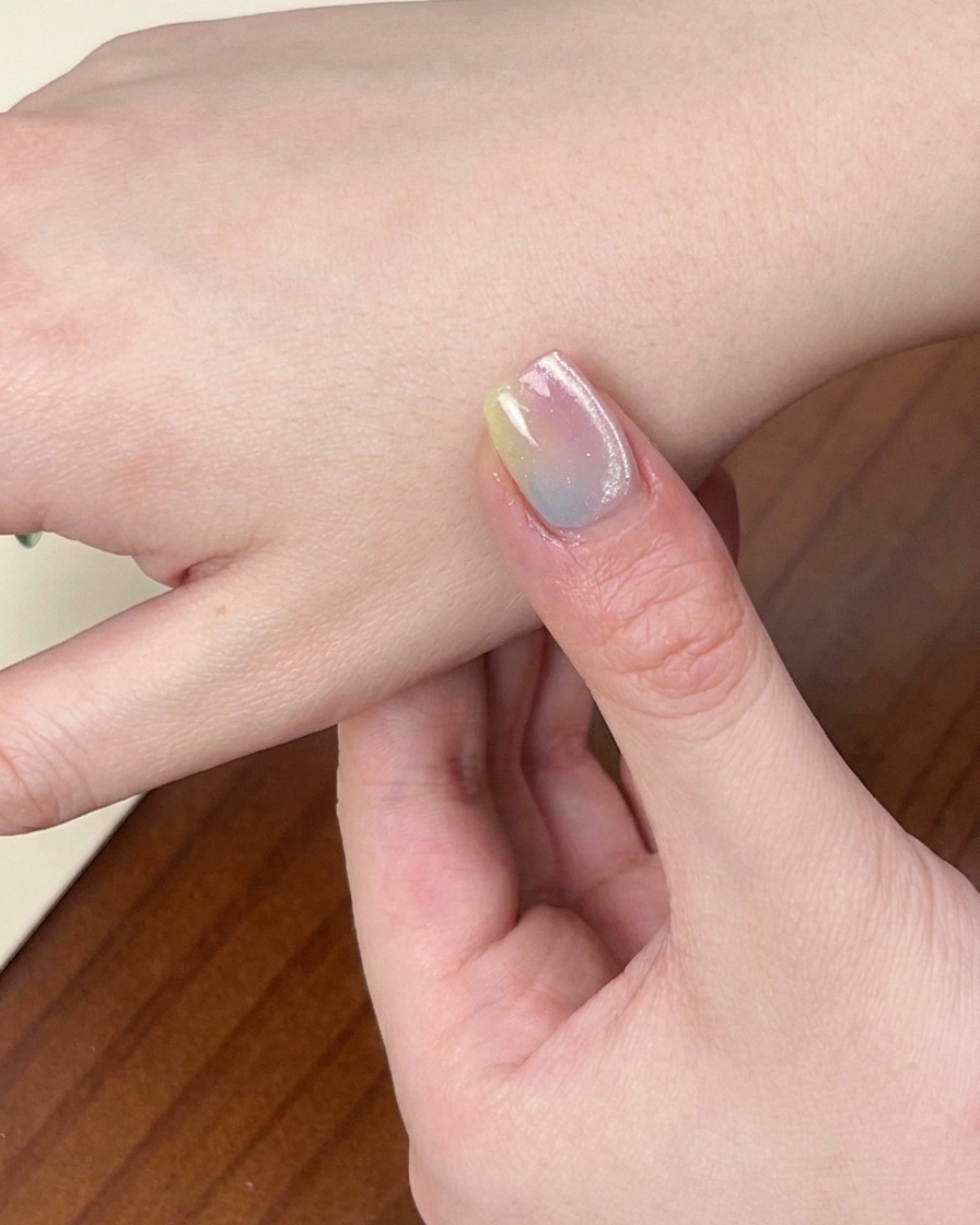 A close-up view of a hand with the finished colorful gradient manicure resting inside a UV/LED nail lamp, with the light active.