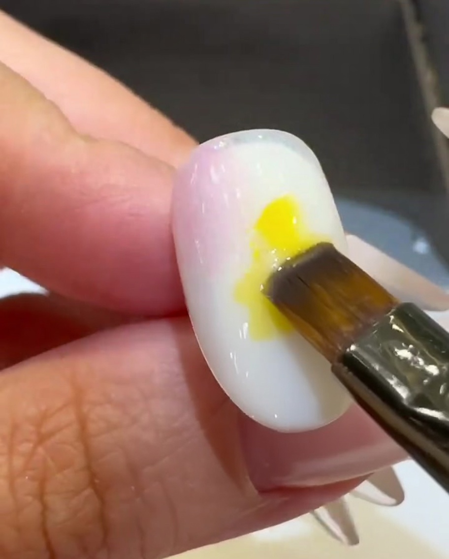 A flat brush placing a drop of bright yellow gel polish onto the center of the nail.