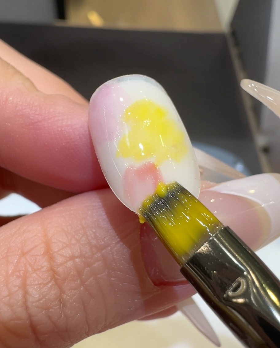 A flat brush blending pink and yellow gel polish on the nail surface.