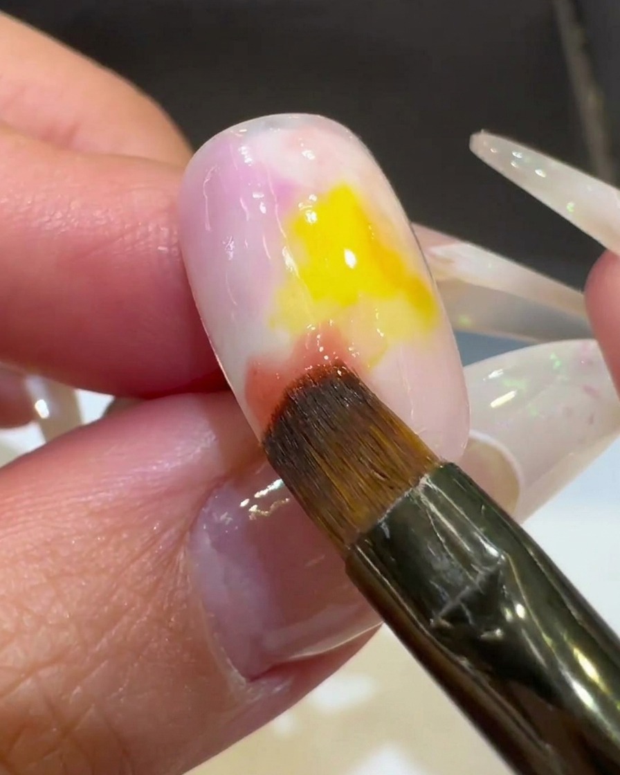 A close-up of a nail brush blending pink gel polish into the yellow center, creating a gradient look.