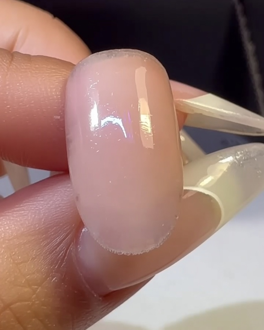 A hand with a multi-colored gradient nail placed inside a UV lamp for the curing process.