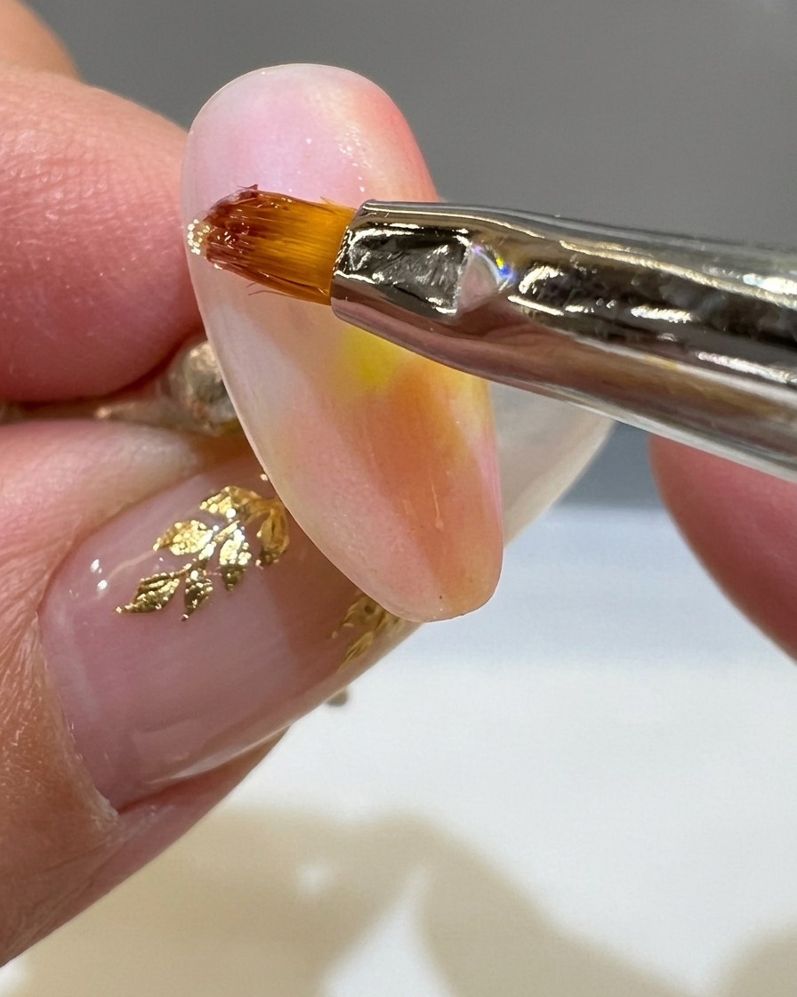 A fine liner brush applying a thick line of clear 3D gel onto a matte sunset-colored nail.