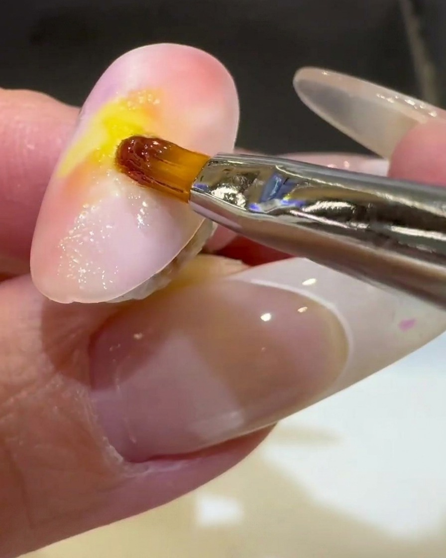 A fine liner brush finishing a clear 3D gel wave on the lower half of a sunset-colored nail.