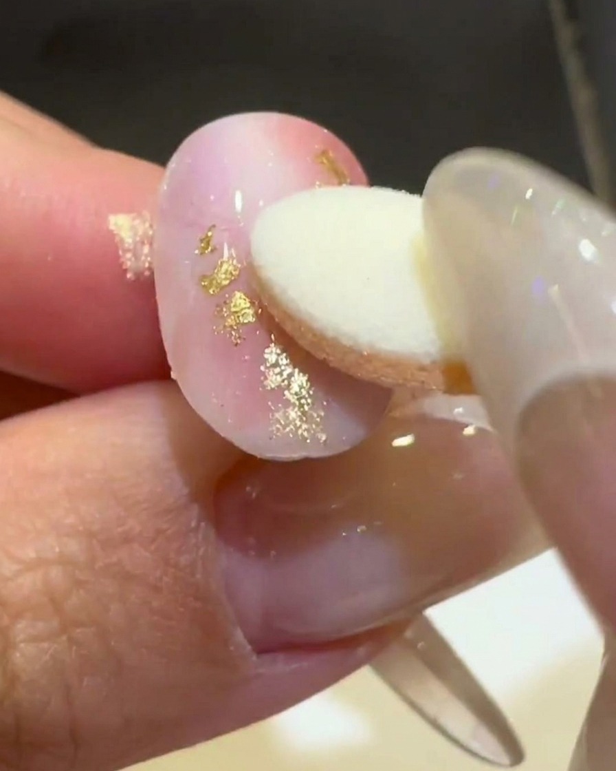 A sponge applicator rubbing gold aurora chrome powder onto a raised 3D wavy line on a matte pink and white nail.