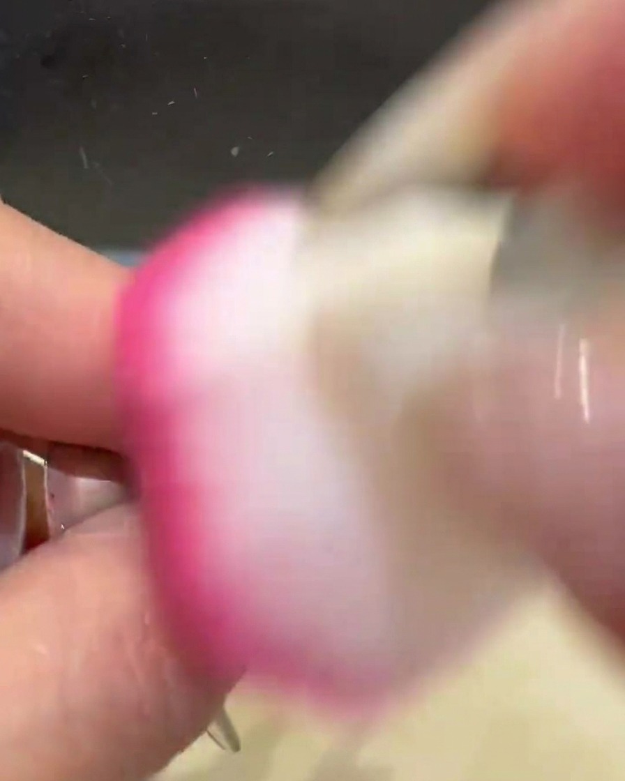 A pink fluffy dusting brush sweeping across a nail to remove excess gold chrome powder.