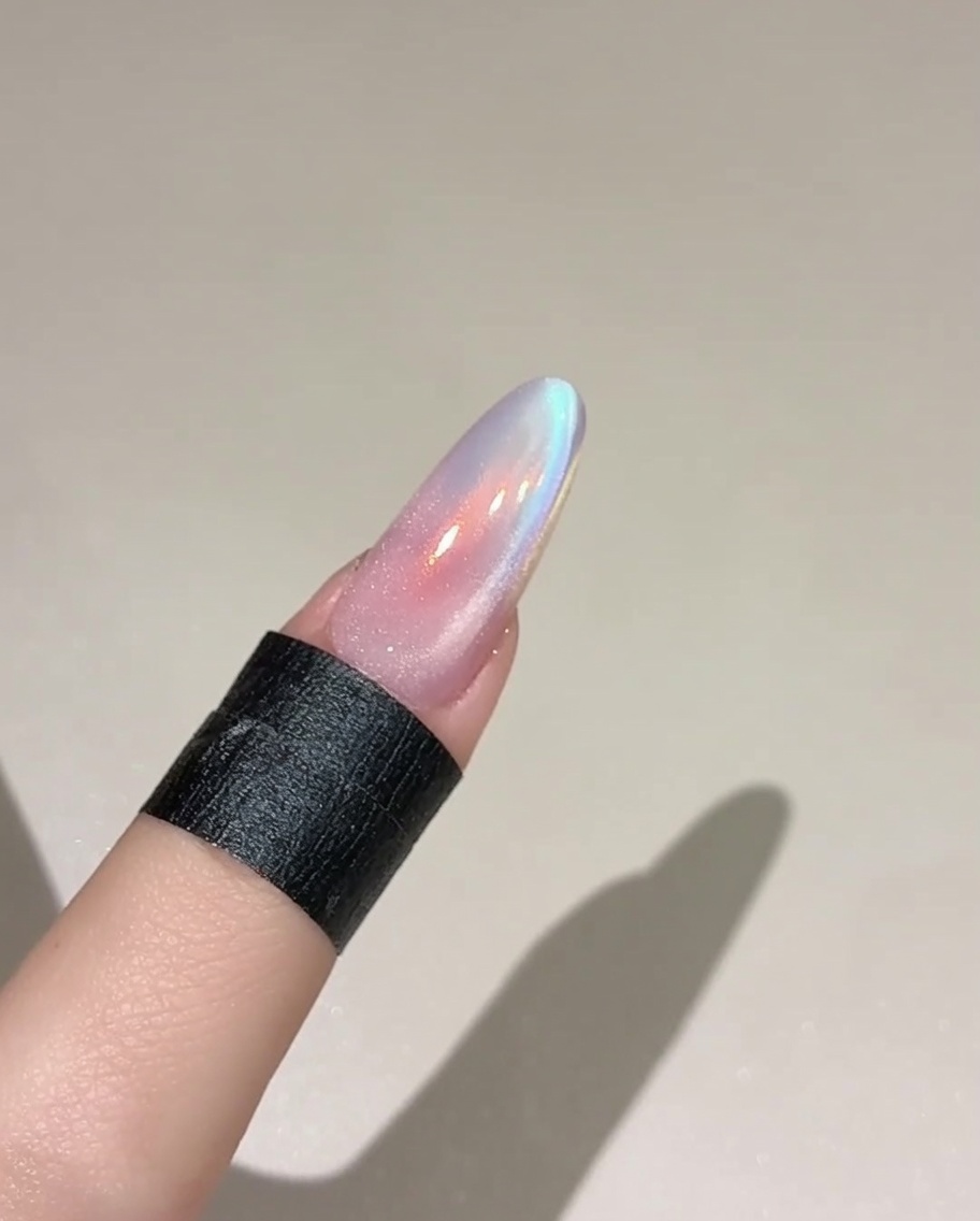 A brush applying a layer of shimmering, translucent cat eye gel onto a nail painted with a base color.