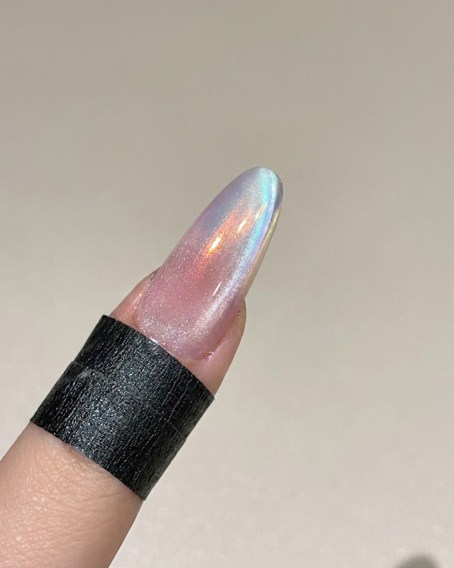 A magnetic tool being held near the side of a fingernail to manipulate the metallic particles in the wet cat eye gel.