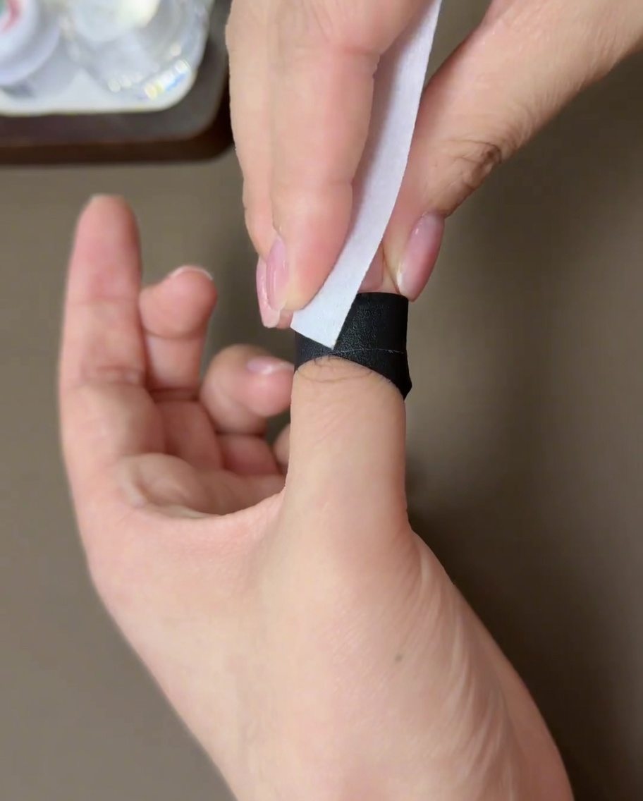 A lint-free wipe being used to clean the surface of a cured gel nail.
