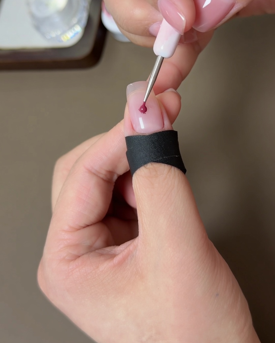 A small tool applying a dot of peach gel polish to the center of a nude nail.