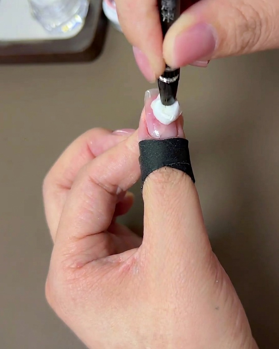 A brush applying a second, more concentrated dot of peach gel over the center of the previous layer.