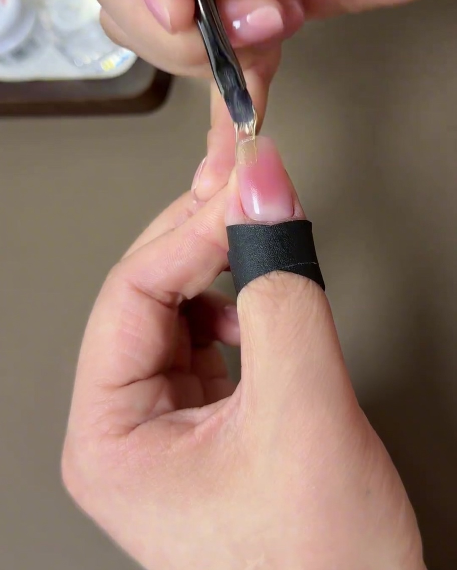A brush applying a coat of shimmery champagne gold magnetic gel to the tip of the nail.