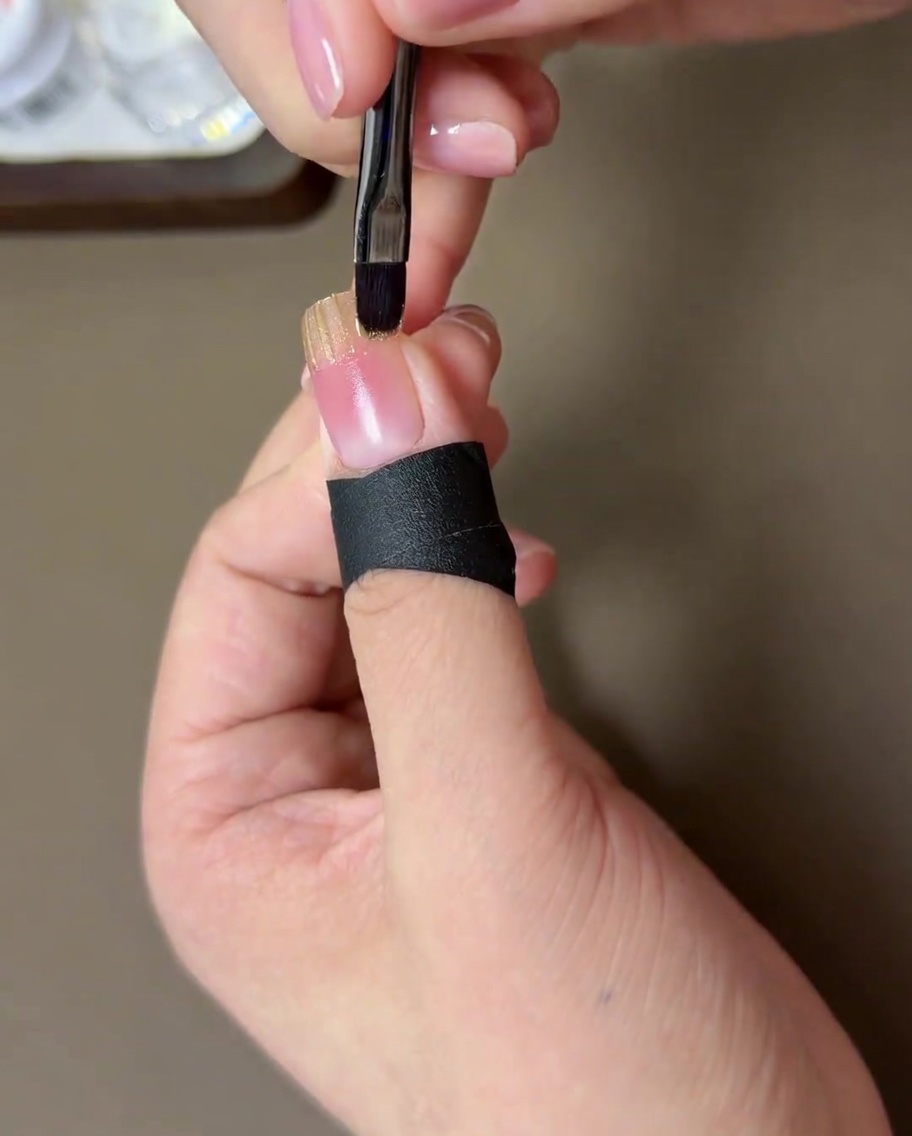 A close-up of a small brush blending the edge of the gold gel into the pink blush base.