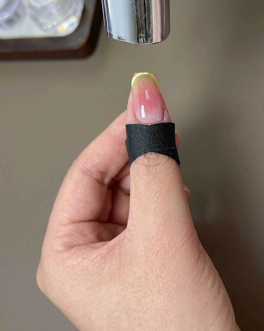 A fingernail with a finished gradient design positioned under a UV nail lamp to cure.