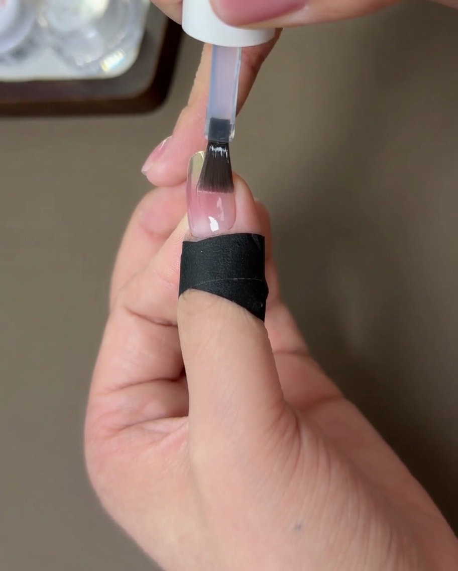 A fingernail finished with a strengthening top coat, being cured under a UV nail lamp.