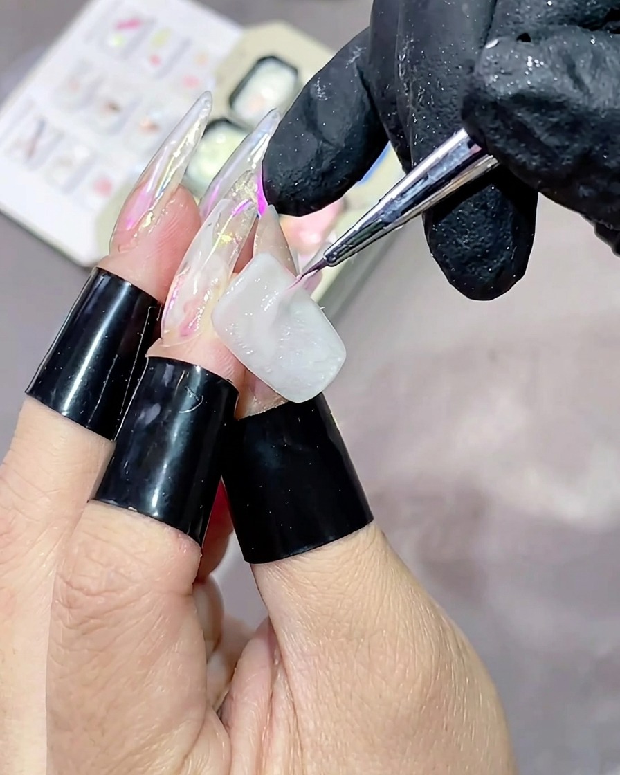 A thin liner brush applying a streak of pink high-gloss texture gel horizontally across a white-painted nail.