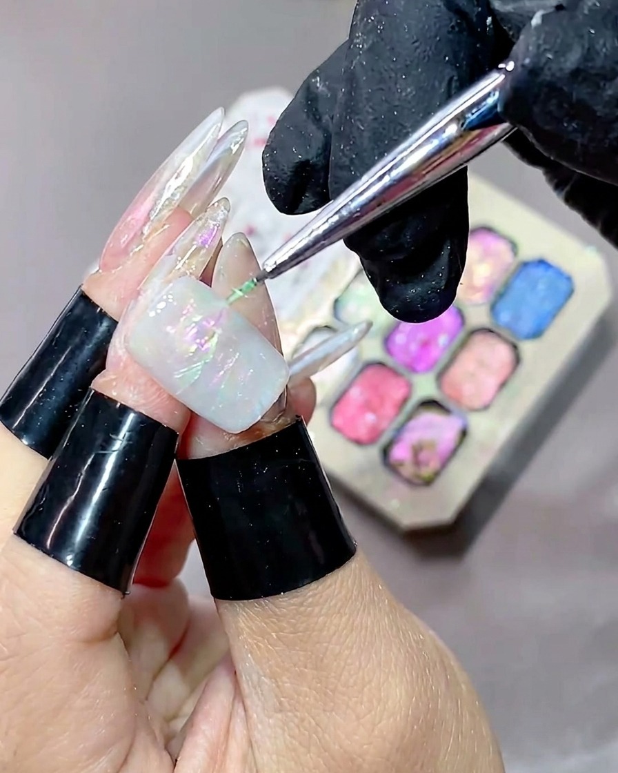 A fine liner brush applying green texture gel across the nail, with a colorful gel palette visible in the blurred background.