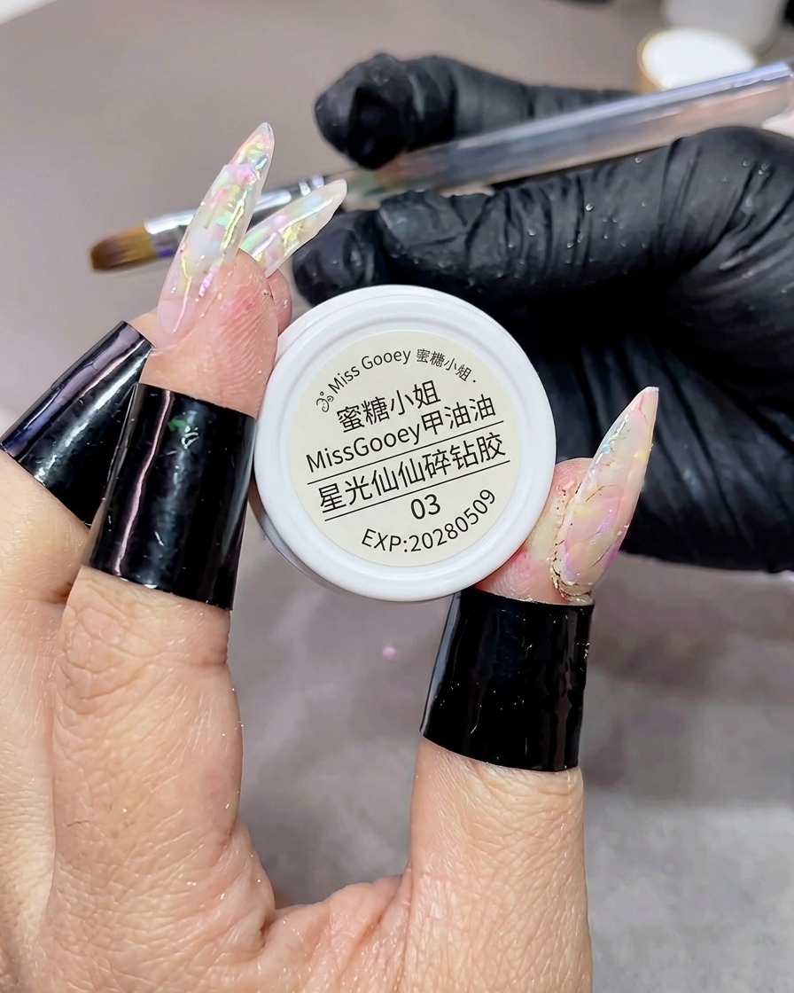 A brush applying star-shaped glitter gel over a textured, marbled gel nail using a back-and-forth Z motion.