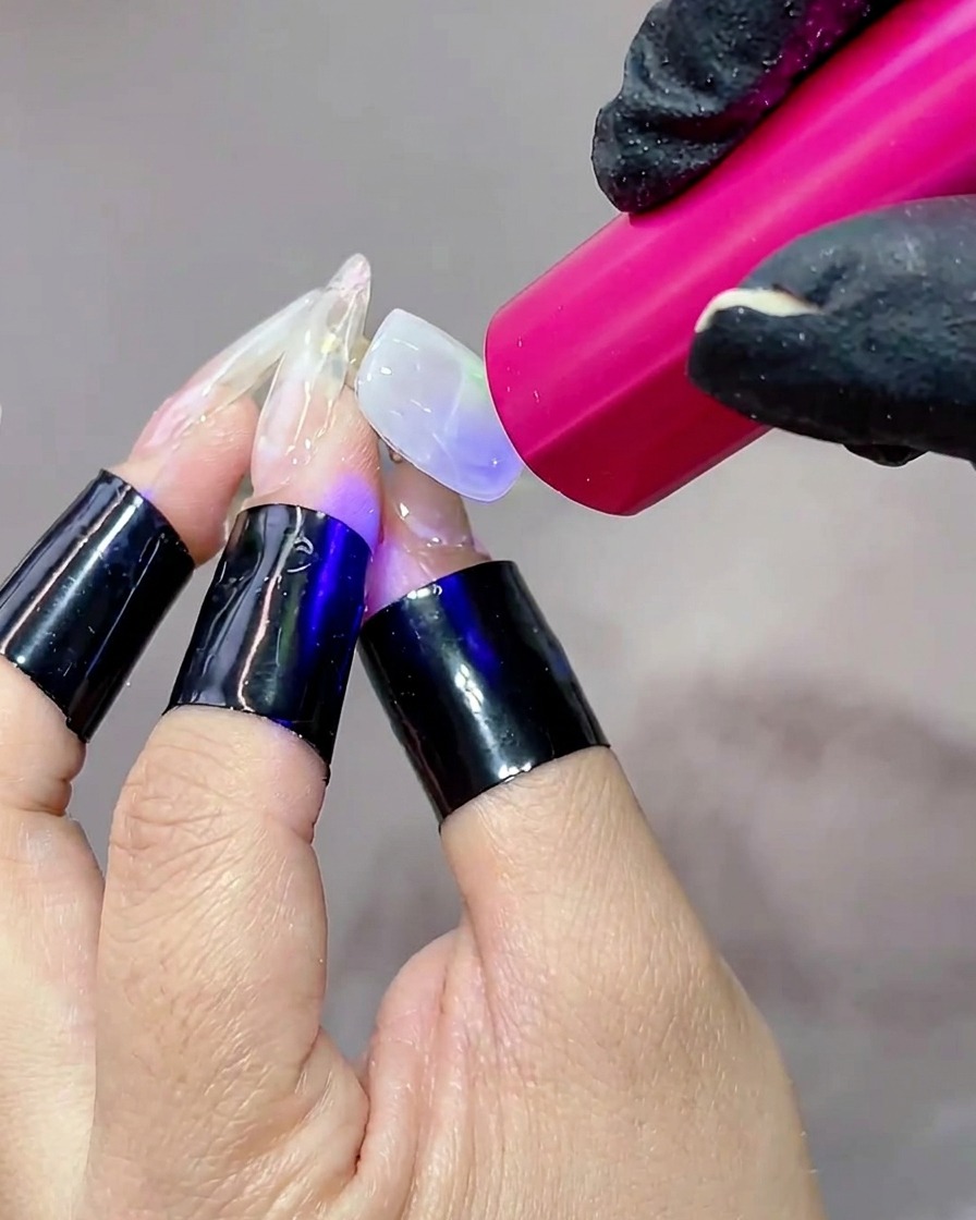 A hand positioned under a portable UV lamp, with the nail surface glowing as the gel cures.
