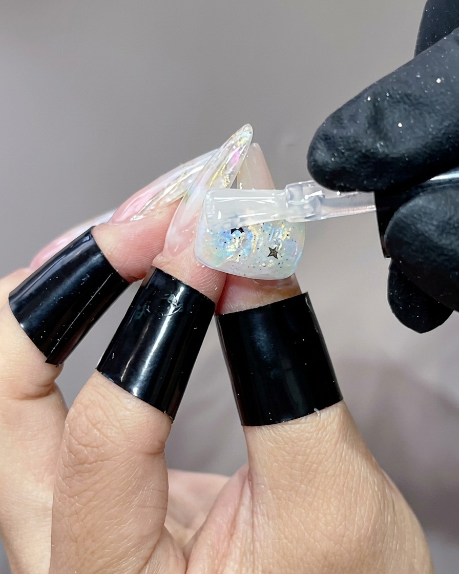 A brush applying a final glossy top coat layer over a finished nail design with star glitters.