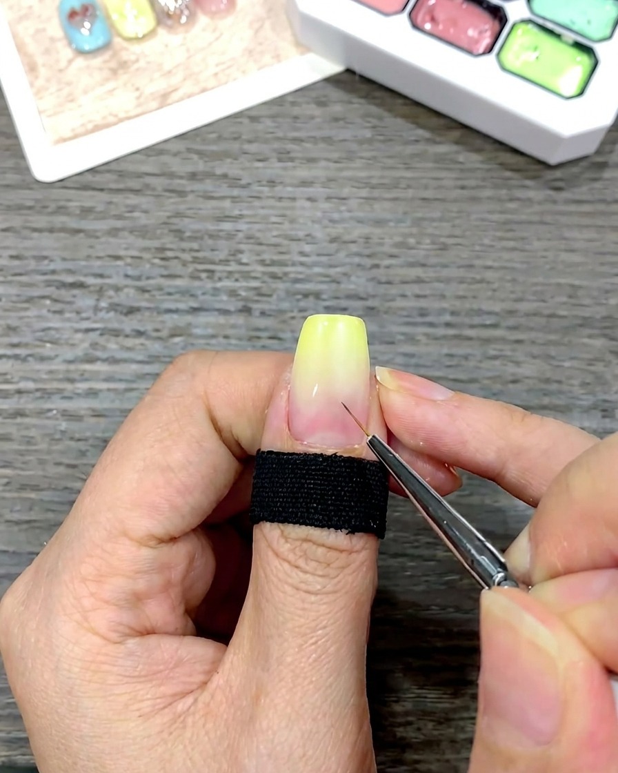 A fine detail brush applying small white guide dots to the center of a nail with a yellow gradient.