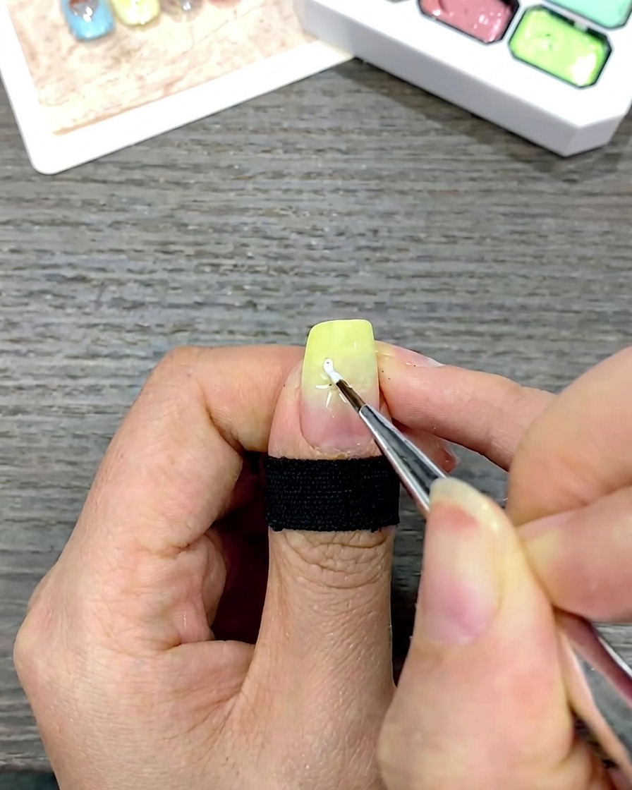 A fine liner brush drawing white daisy petals by pulling gel toward the center of the nail.
