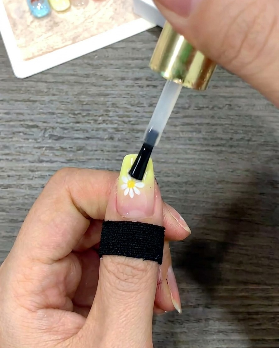 A close-up shot of a nail brush smoothing a layer of glossy top coat over the entire surface of the nail.