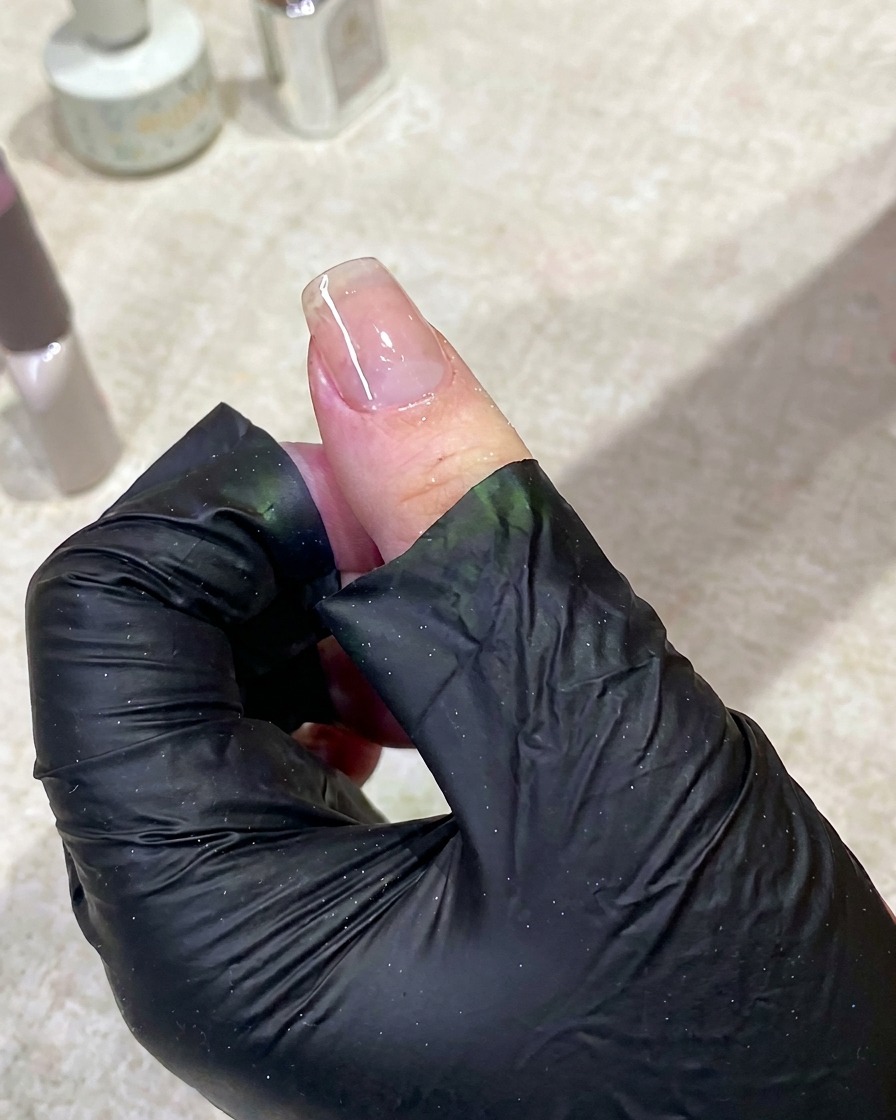 A hand resting inside a UV nail lamp with the light on, curing the base coat.