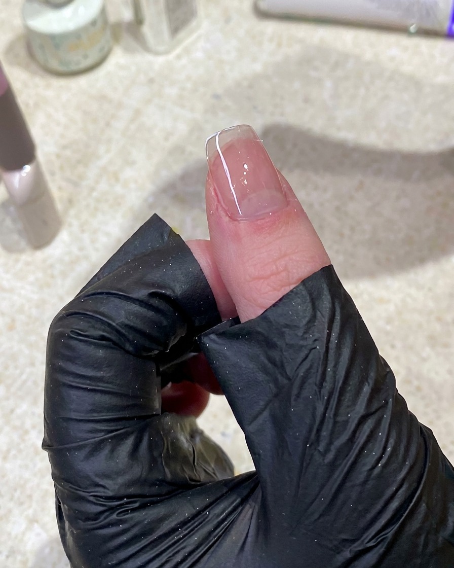 A close-up of a hand using a lint-free wipe to clean the surface of a manicured nail.