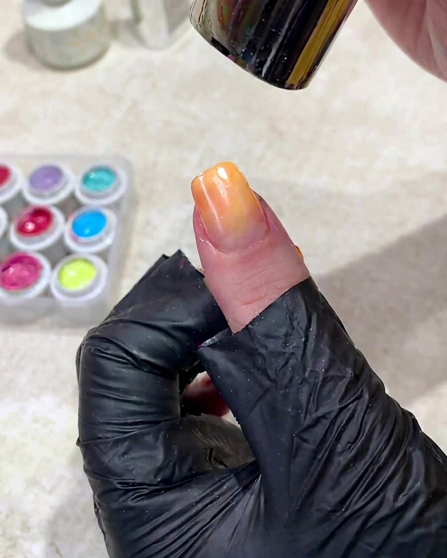 A hand positioned under a UV nail lamp to cure the freshly applied gradient gel.